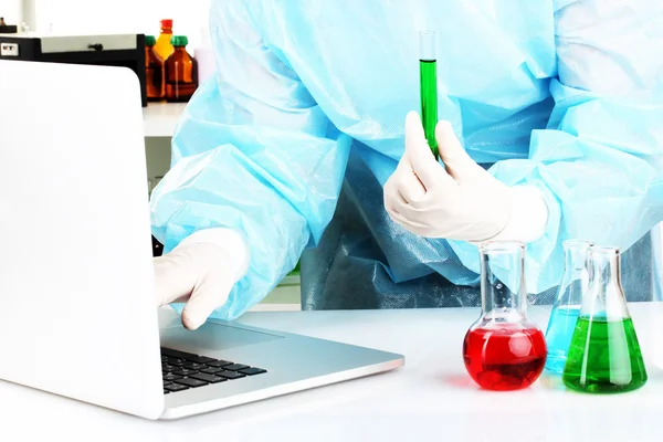 Scientist entering data on laptop computer with test tube close up