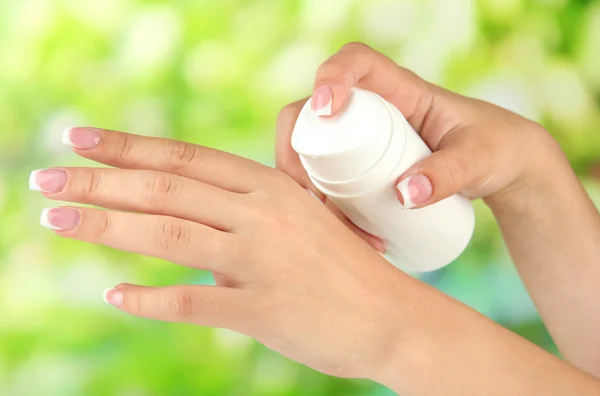 Woman applying cream on hands on bright background