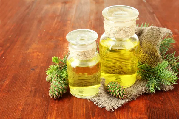 Bottles of fir tree oil and green cones on wooden background