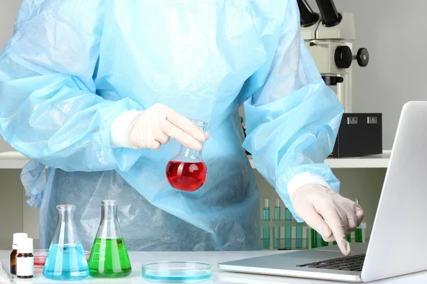 Scientist entering data on laptop computer with test tube close up