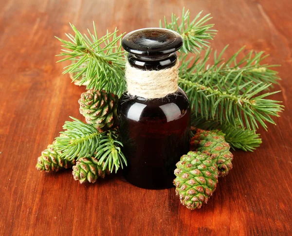 Bottle of fir tree oil and green cones on wooden background