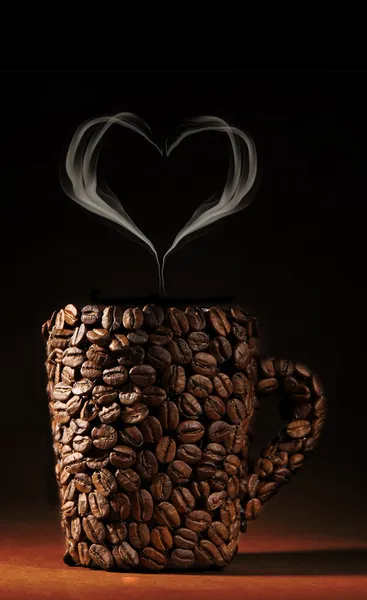 Cup of coffee beans with smoke in shape of heart on brown background