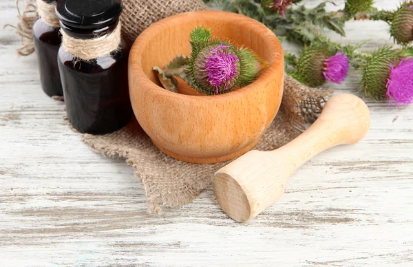 Medicine bottles and mortar with thistle flowers on wooden background