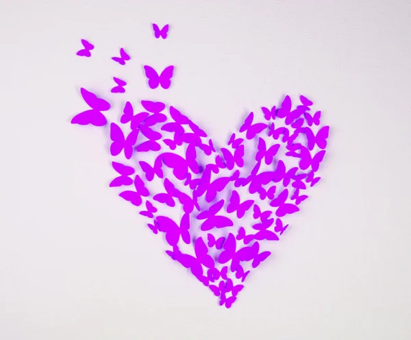 Paper purple butterfly in form of heart on wall