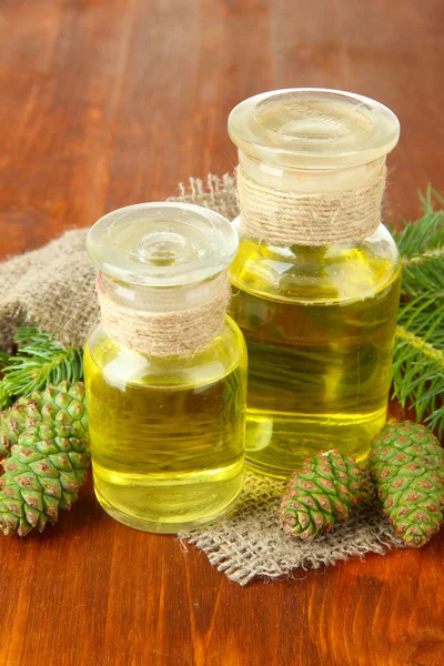 Bottles of fir tree oil and green cones on wooden background