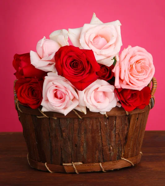 Beautiful bouquet of roses in wooden basket on table on pink background
