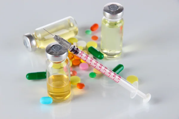 Medical bottles syringe and tablets on light gray background