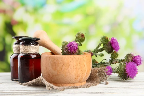 Medicine bottles and mortar with thistle flowers on nature background