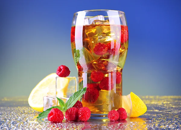 Iced tea with raspberries and mint on blue background
