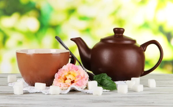 Kettle and cup of tea from tea rose on board on napkin on wooden table on nature background