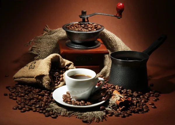 Cup of coffee, grinder, turk and coffee beans on brown background