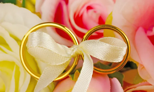 Wedding rings tied with ribbon on rose background