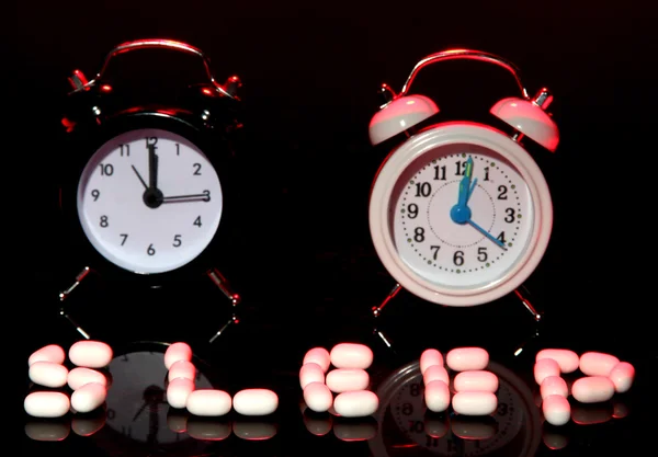 Old style alarm clocks and pills, on dark background