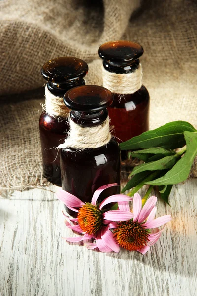 Medicine bottles with purple echinacea flowers on wooden table with burlap