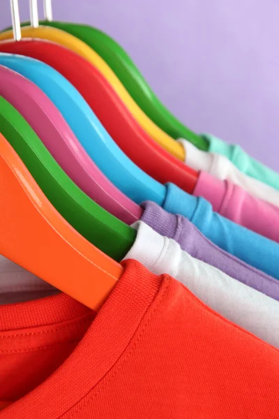 Different shirts on colorful hangers on purple background