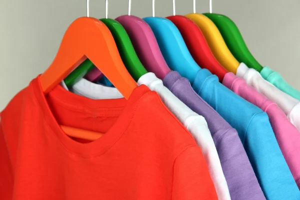 different shirts on colorful hangers on grey background