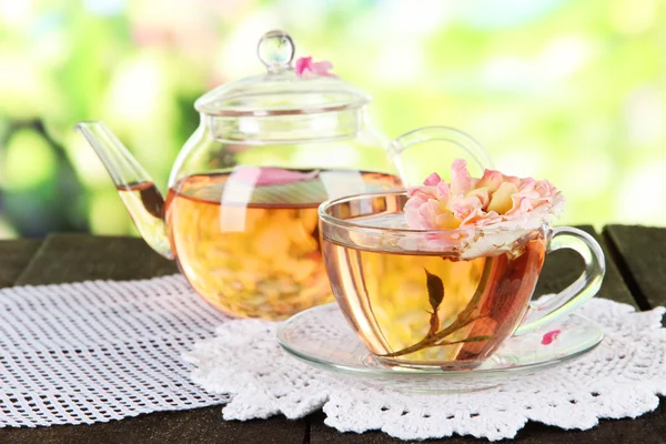 Kettle and cup of tea from tea rose on napkin on wooden table on nature background