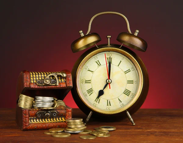 Antique clock and coins on wooden table on dark color background