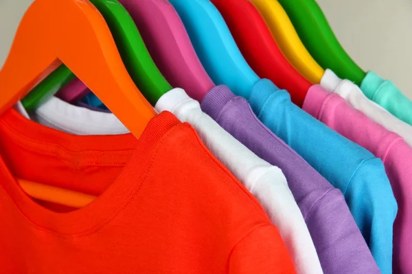 different shirts on colorful hangers on grey background