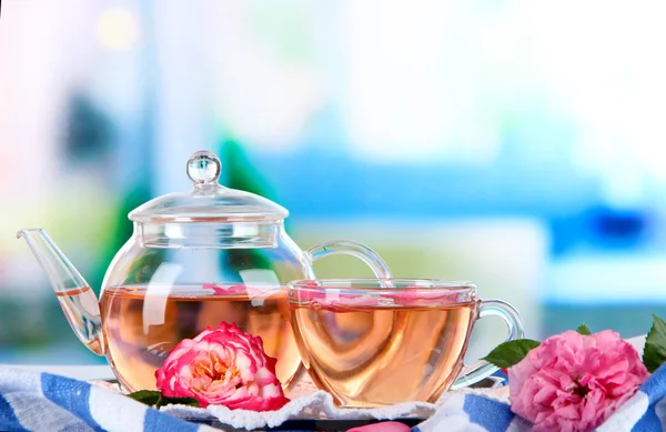 Kettle cup of tea from tea rose on metallic tray on tablecloth