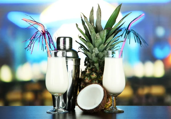 Pina colada drink in cocktail glasses and metal shaker, on bright background