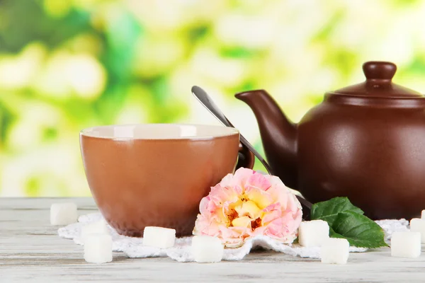 Kettle and cup of tea from tea rose on board on napkin on wooden table on nature background