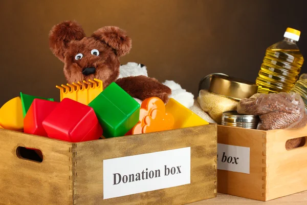 Donation box with food and children\'s toys on brown background close-up