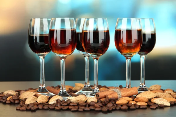 Glasses of liquors with almonds and coffee grains, on bright background