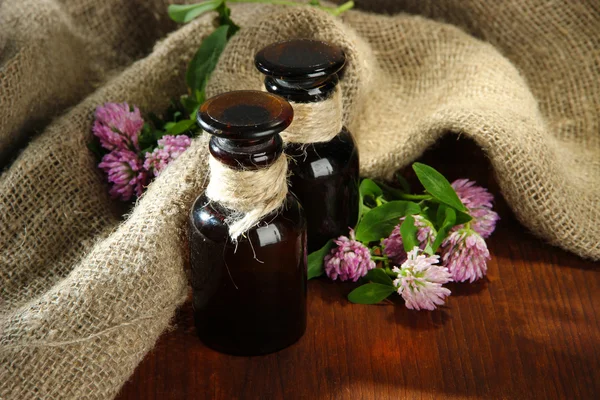 Medicine bottles with clover flowers on wooden table with burlap