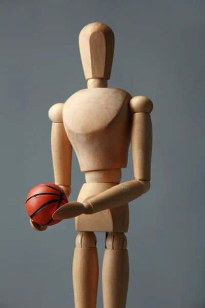 Wooden mannequin with basketball ball on grey background