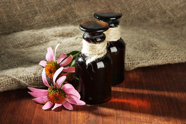 Medicine bottles with purple echinacea flowers on wooden table with burlap