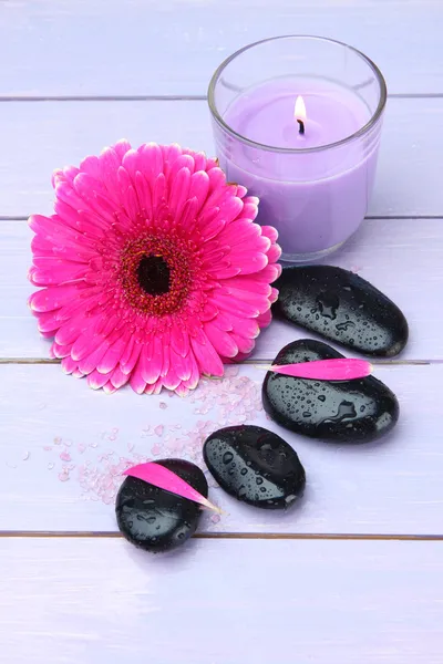 Spa stones, beautiful gerbera and candle on wooden table
