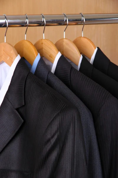 Suits with shirts on hangers on wooden background