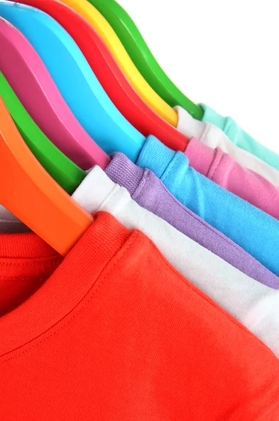 Different shirts on colorful hangers on white background