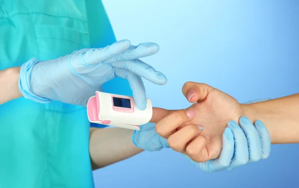 Doctor measuring pulse rate and oxygen levels, on color background