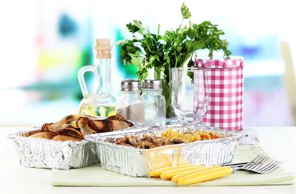 Food in boxes of foil on tablecloth on window background