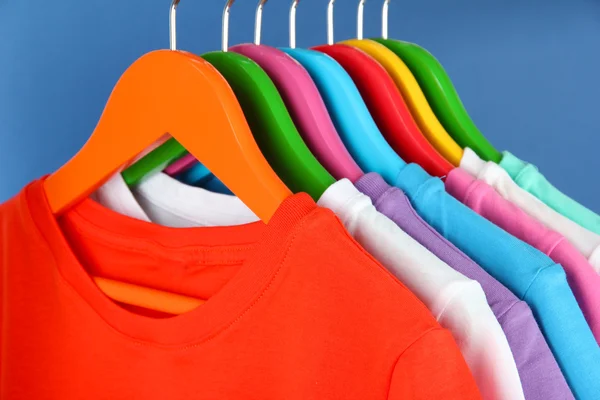 different shirts on colorful hangers on blue background