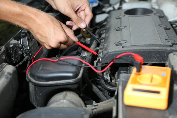 Auto mechanic uses multimeter voltmeter to check voltage level in car battery