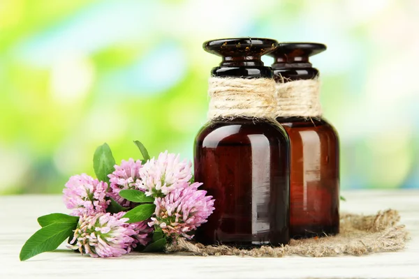 Medicine bottles with clover flowers on wooden table, outdoors