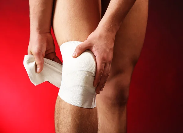 Young man with elastic bandage on knee, on red background