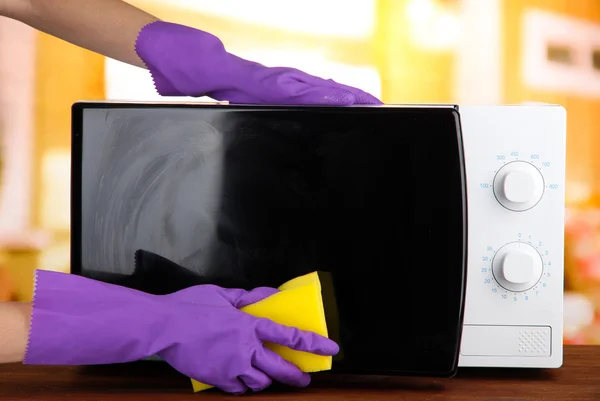 Hand with sponge cleaning microwave oven, on bright background