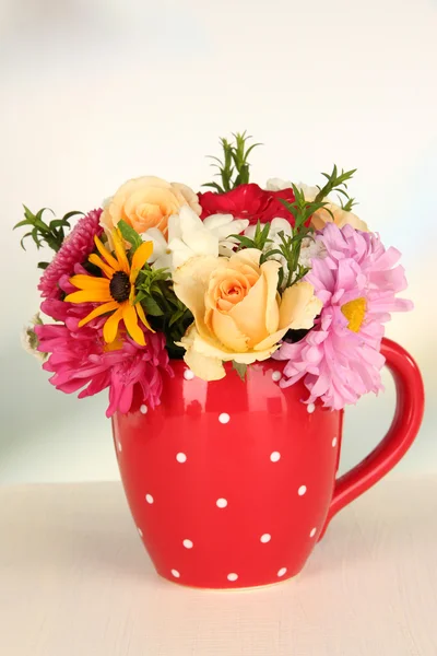 Beautiful bouquet of bright flowers in color mug, on wooden table, on light background