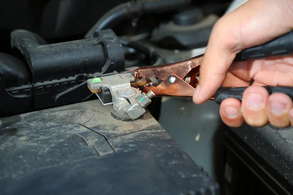 Car mechanic uses battery jumper cables to charge dead battery