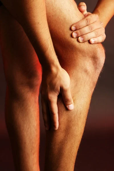 Young man with knee pain on dark background