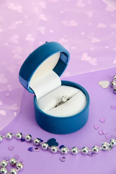 Beautiful box with wedding ring on purple background