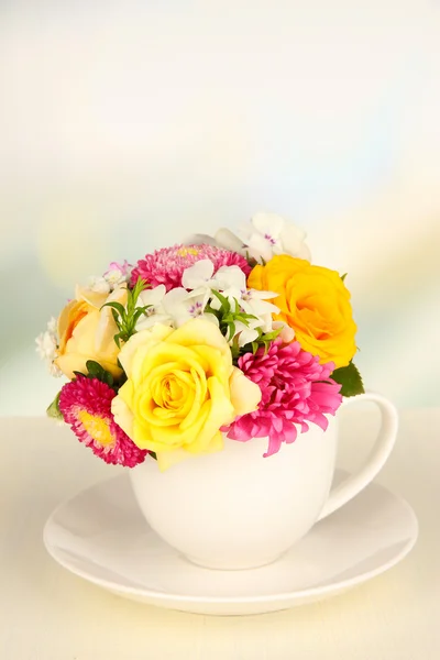 Beautiful bouquet of bright flowers in color mug, on wooden table, on light background
