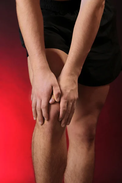 Young man with knee pain, on red background