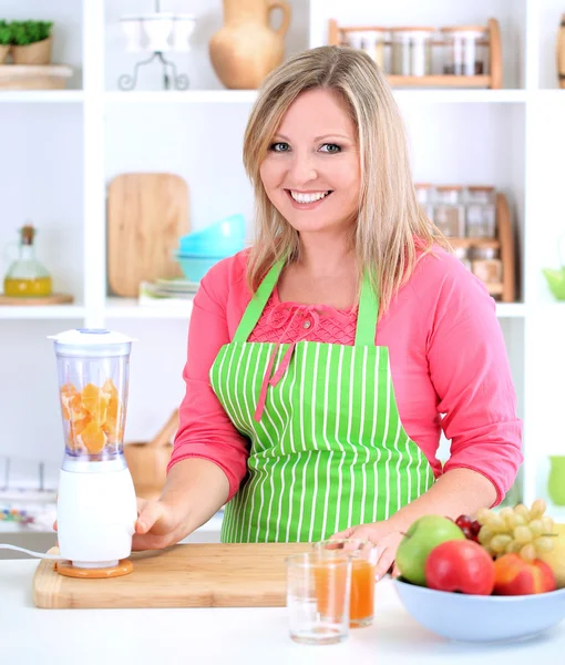 Happy smiling woman in kitchen preparing fresh fruit cocktail