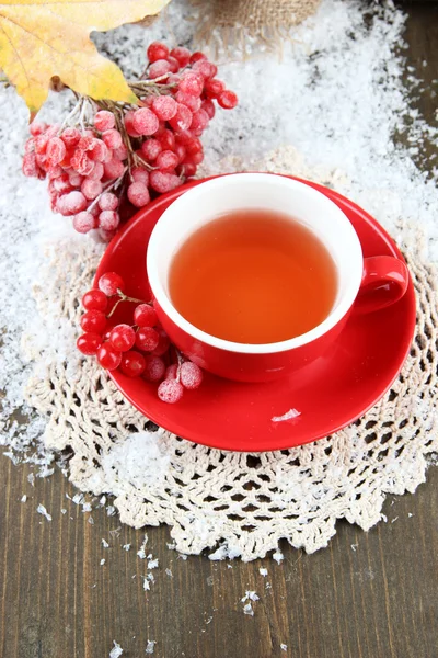 Still life with viburnum tea in cup, berries and snow, on wooden background