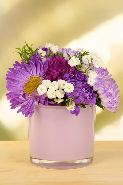 Beautiful bouquet of bright flowers in glass vase, on wooden table, on bright background